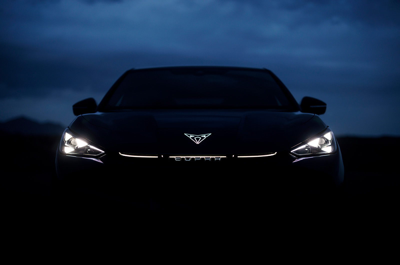The front of a Cupra Tavascan in the dark with just the illuminated emblem and headlights visible