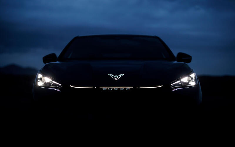 The front of a Cupra Tavascan in the dark with just the illuminated emblem and headlights visible