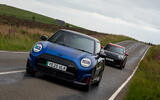 A black and red MINI John Cooper Works Aceman follows a blue and black MINI John Cooper Works Electric down a long straight country road in the peak district