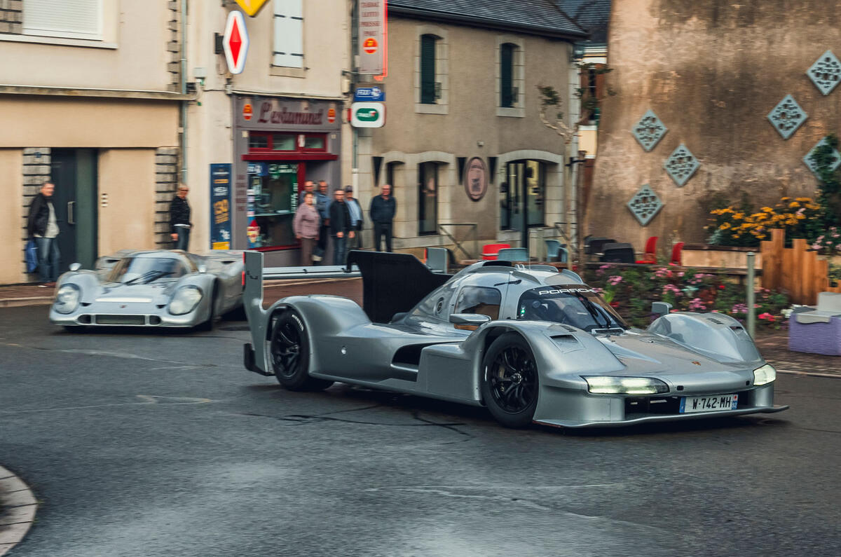 Porsche 963 RSP with 917 driving through town front quarter tracking